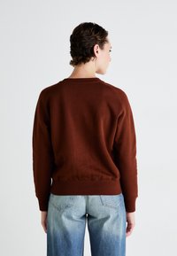 Sudadera marrón con cuello redondo y puños acanalados, combinada con jeans de tiro alto en azul claro. Tela suave con un diseño minimalista.