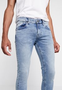 Ljusblå denimjeans med slim fit, med framfickor, subtil blekning och dragkedjestängning. Tyget har en slät yta.