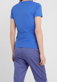 Kortärmad blå t-shirt i bomull, med klassisk rundad halsringning och en mjuk textur, ihop med lila byxor.