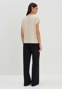 Top leggero beige chiaro a maniche corte con tessuto testurizzato, una vestibilità comoda e scollatura rotonda, abbinato a pantaloni neri larghi. Design semplice.