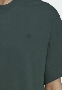 Dunkelgrünes T-Shirt mit kurzen Ärmeln und kleinem gesticktem Logo auf der linken Brust sowie rundem Halsausschnitt.