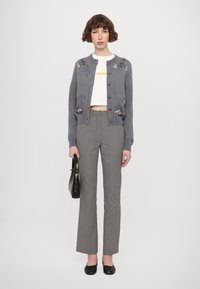 Cardigan gris brodé avec des motifs floraux, top croppé blanc, pantalon évasé noir et blanc à motifs, et sac à main noir. Chaussures plates noires.