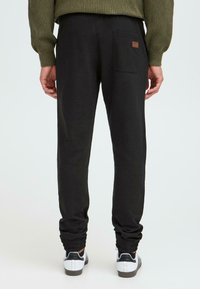 Black sweatpants with elastic cuffs, back pocket detail, and a small logo. Material appears soft with a smooth texture.