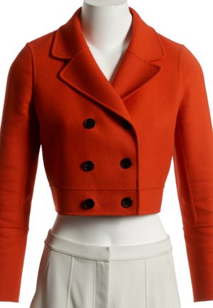 Veste orange courte croisée à doubles boutons noirs associée à un pantalon blanc plissé taille haute sur un mannequin.