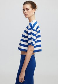 Top recortado con rayas horizontales en azul y blanco, mangas cortas y escote redondo. Combinado con pantalones de tiro alto en azul sólido.