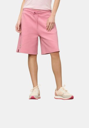 Kvinde iført pastelrosa knælange shorts med snøre i taljen og lyserøde sneakers, stående på en hvid baggrund.