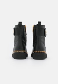 Botas de tobillo de cuero negro con detalles en cremallera dorada, costuras texturizadas a lo largo de la suela y tiradores en la parte posterior para facilitar su uso.