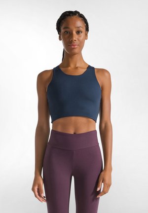 Navy crop top yang terbuat dari kain elastis dengan leher bulat dan tali lebar, dipadukan dengan legging ungu gelap berpinggang tinggi.