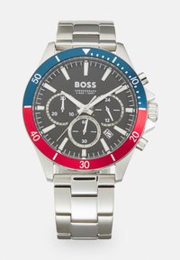Montre chronographe en acier inoxydable avec un cadran noir, une lunette rouge et bleue, des aiguilles en ton argent et trois sous-cadrans. Elle possède une fenêtre de date à 6 heures.
