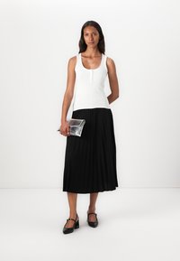 White ribbed tank top with a front button detail, paired with a black pleated midi skirt. Holding a silver clutch, wearing black shoes.