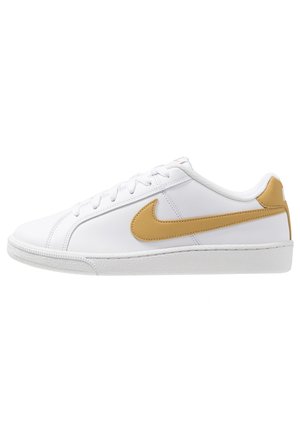 Baskets basses blanches avec un swoosh Nike beige et un détail au talon, lacets blancs et semelle blanche texturée, vue de côté.