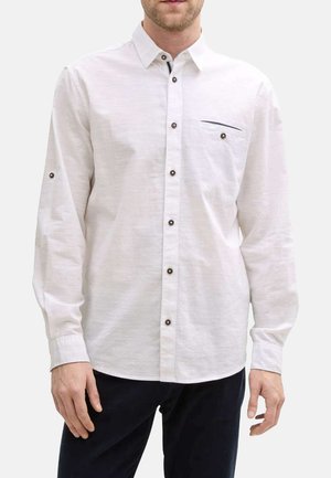 Chemise blanche à manches longues en tissu texturé, dotée de boutons marron, d'un col boutonné et d'une poche poitrine avec un détail de couture horizontale.