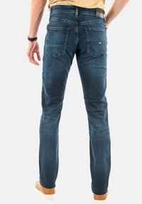 Vaqueros de mezclilla azul oscuro con un ajuste Slim, que cuentan con dos bolsillos traseros y una etiqueta en la cinturilla. Textura suave y un ligero desvanecimiento.