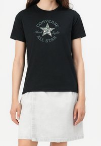 Camiseta negra de algodón con un gráfico de estrella floral y el texto "Converse Chuck Taylor All Star". Con mangas cortas y corte relajado.