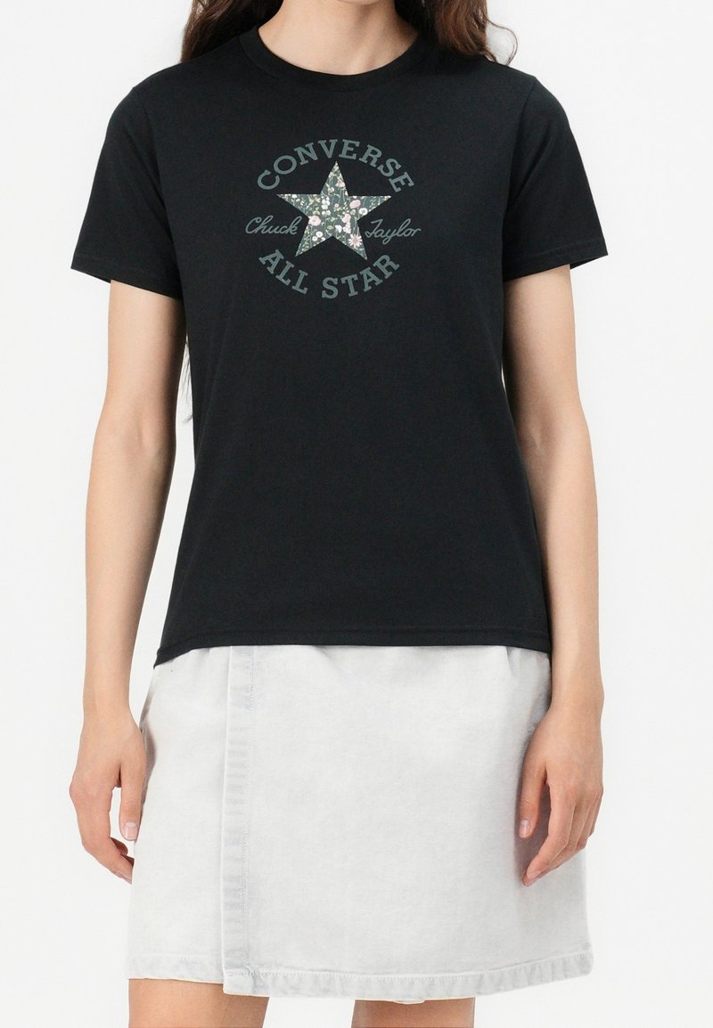 Camiseta negra de algodón con un gráfico de estrella floral y el texto "Converse Chuck Taylor All Star". Con mangas cortas y corte relajado.