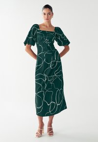 Roheline kleit koos puhvli varrukatega, ruudukujulise dekolteega ja valgete abstraktsete joonistega. Valmistatud siledast kangast, põlvekõrgune ja kinnitatud taljega.