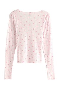 Lyserød bluse med lange ærmer og ribbet tekstur; har små lyserøde sløjfer og prikker i et gentagende mønster over det hele.