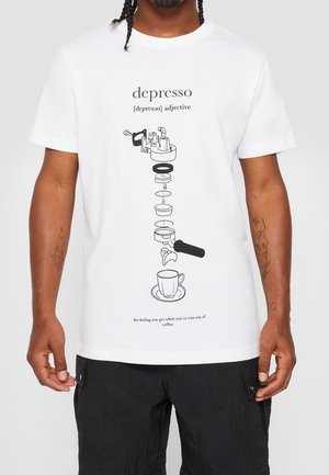 Hombre con camiseta blanca con partes de cafetera explotadas sobre una taza y texto que define "depresso" como quedarse sin café.