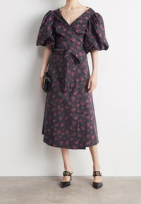 Czarna sukienka w kwiaty z bufkami, wiązaniem w talii, długości do kolan, z różowymi wzorami kwiatów. Połączona z czarnymi szpilkami.