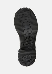 Suela de zapato de goma negra con textura estriada elevada, logo "CAMPER" en relieve, marcador de tamaño circular "38" y agarre con patrón.