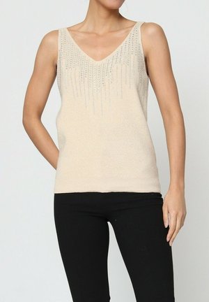 Haut sans manches beige avec un col en V, orné de sequins argentés verticaux et d'une texture douce, associé à un pantalon noir ajusté.