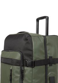 Maleta de ruedas verde y negra con una superficie texturizada, bolsillos con cremallera, un asa superior y un asa retráctil para mayor movilidad.