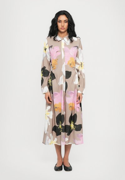 Robe florale avec un fond marron clair, ornée de grandes fleurs roses, blanches, jaunes et noires, à manches longues et avec un col.