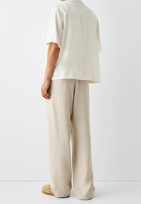 Losse, kortom mouwloze blouse van crème stof, gecombineerd met lichtbeige, wijde broeken. Heeft een zachte, gladde textuur en een subtiele val.