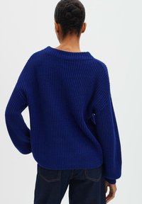Pull en grosse maille bleu vif, avec un large col, une coupe décontractée et des manches longues à côtes. Texture douce avec des mailles ouvertes.