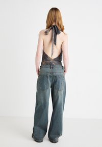 Vista traseira de uma pessoa vestindo um top de halter preto e cinza com padrão e jeans largos, de perna larga, desbotados, em azul, com tachas decorativas nos bolsos.