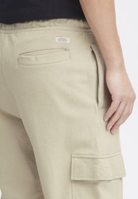 Beige cargobroek met een textuurafwerking, voorzien van zijzakken, een zichtbaar label op de tailleband en een ontspannen pasvorm.