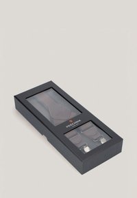 Brązowe materiałowe szelki z skórzanymi akcentami i metalowymi klipsami, zaprezentowane w czarnym pudełku z przezroczystym przodem, opatrzone etykietą "PROCHNIK."