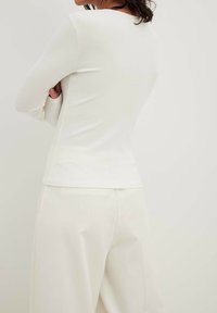 Maglietta bianca a maniche lunghe con scollatura rotonda, forma aderente e tessuto testurizzato, abbinata a pantaloni larghi color crema.