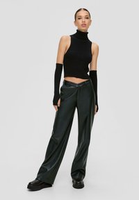 Schwarzer gerippter Rollkragen-Crop-Top kombiniert mit hoch taillierten, dunkelgrünen, faux ledernen, weiten Hosen und schwarzen Plateau-Schuhen.