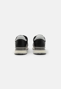 Zapatillas deportivas negras con parte superior de cuero suave, acentos grises en el talón y amortiguación transparente. Etiquetadas con "GUESS" en el talón.