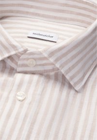 Col de chemise beige et blanc rayé avec deux boutons blancs et une étiquette "seidensticker" à l'intérieur du col.