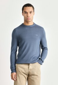 Light blue sweater made of knit fabric, featuring a round neckline and ribbed cuffs. Small logo displayed on the chest.