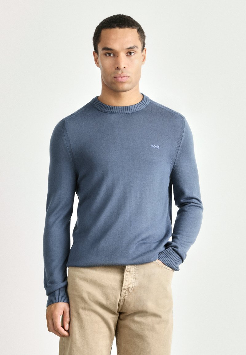 Light blue sweater made of knit fabric, featuring a round neckline and ribbed cuffs. Small logo displayed on the chest.