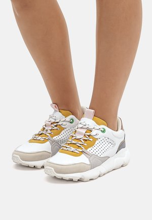 Zapatillas blancas y grises con acentos en amarillo y marrón claro, que cuentan con detalles de malla, cordones redondos y una suela de goma gruesa.