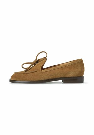 Mocassino in suede marrone con dettaglio a fiocco sulla parte superiore, suola piatta scura e tacco basso, mostrato in prospettiva laterale su sfondo bianco.