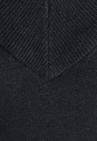 Pull noir en maille avec un col en V, présentant une texture côtelée et un motif en chevrons. Tissu doux et dense offrant de la chaleur.