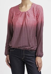 Top a maniche lunghe con un motivo a gradiente di pois rosa e bianchi che sfumano in rosso scuro. Presenta un collo rotondo e dettagli arricciati sul davanti.