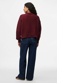 Bordeaux gebreide trui met een ontspannen pasvorm, geribde mouwen en zoom. Gepaarde met blauwe denim jeans met wijde pijpen en bruine schoenen.
