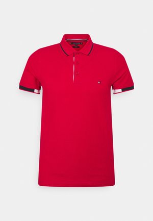 Polo rossa a maniche corte con patta a tre bottoni, righe bianche e nere sui bordi delle maniche e del colletto, e un piccolo logo sul petto.