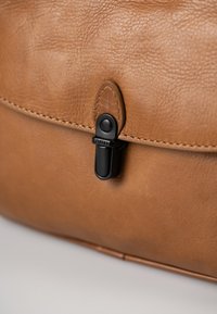 Brown leather bag with a textured surface, featuring a black clasp and stitching detail along the flap.