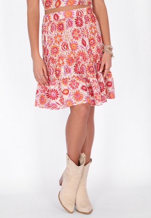 Vrouw draagt een roze en oranje bloemenrok met crèmekleurige laarzen die tot halverwege de kuit reiken en armbanden om haar linker pols.