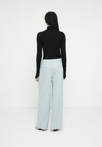 Fekete hosszú ujjú garbó világoskék, bőszárú nadrággal párosítva. A nadrág sima textúrájú, hátul zsebekkel. Egyszerű dizájn.