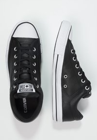 Černé kožené tenisky s nízkým designem, bílým gumovým krytem špičky, dírkami na šněrování a podrážkou s černými akcenty. Viditelné klasické branding Converse All Star.