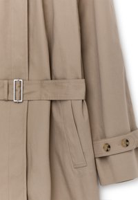 Beżowy płaszcz trencz z paskiem zapinanym na prostokątną srebrną klamrę, boczną kieszenią oraz paskiem na rękawie z dwoma guziczkami w kolorze żółwia.