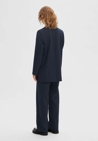 Marineblauw op maat gemaakte pak van textuurstof, met een enkel-breasted blazer met knopen en een broek met wijdere pijpen.